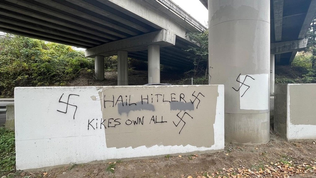 Graffiti on a concrete barrier showing swastikas and the phrases “Hail Hitler” and “Kikes own all.”