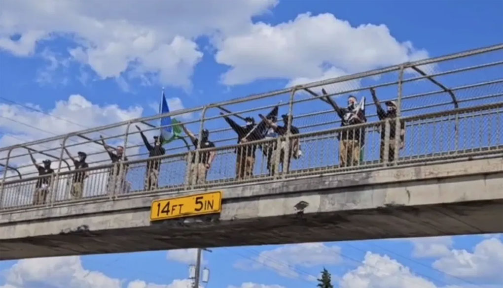 A group of people standing on an overpass holding flags and giving a Nazi salute.