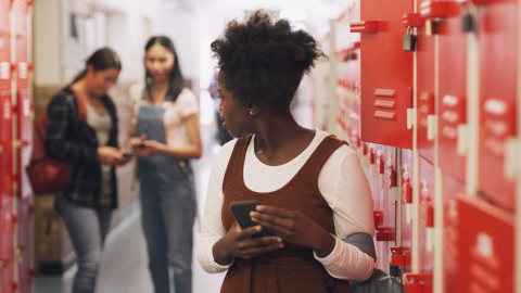 Teenage girl standing next to her school locker using a smartphone and being bullied